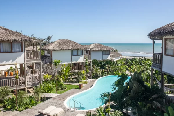 Aerial view of Yemanja with thatched-roof bungalows, curved pool and ocean