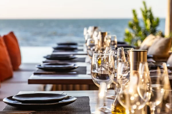 Row of set tables at Yemanja with wine glasses and ocean view at dusk