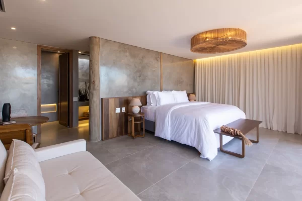 Spacious suite with king size bed, sofa, rattan chandelier and polished concrete walls in warm tones