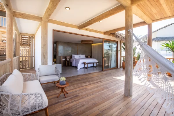Large wooden terrace with hammock, lounge chairs and view into the open room with exposed wooden beams