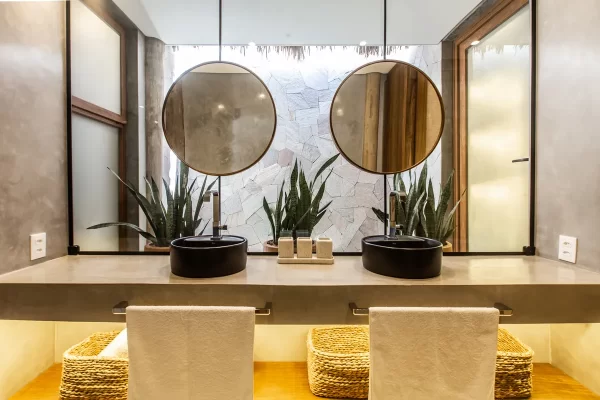 Bathroom with double black basin on concrete countertop, round mirrors and natural stone wall